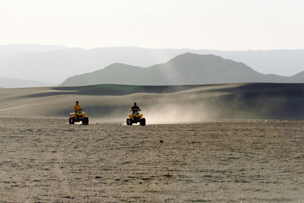 Two people riding ATVs across a scenic desert landscape, leaving dust trails in their wake.